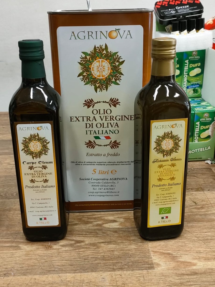 Le bottiglie Agrinova da tre quarti di litro sul banco della bottega — il Carpe Oleum extravergine e l’Aureum Oleum biologico — davanti alla latta da cinque litri della cooperativa