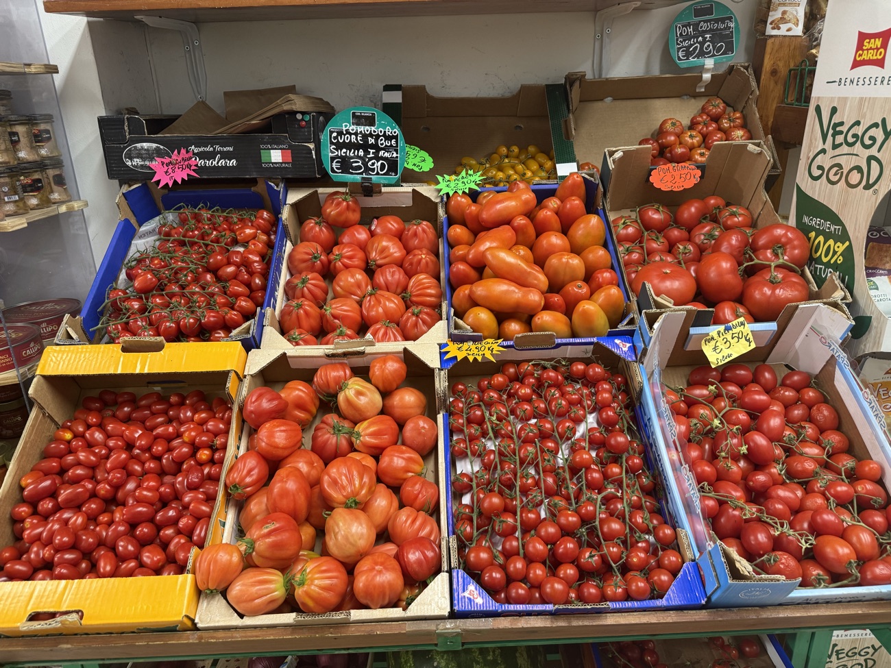 Cassette di pomodori freschi — cuore di bue, ciliegino e datterino — sul banco della bottega
